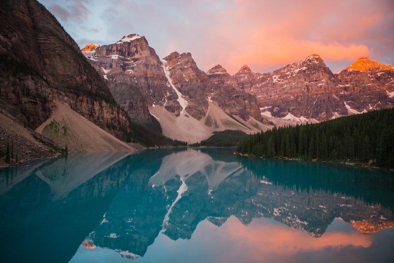 A still lake reflecting mountains and forest under an early sky.