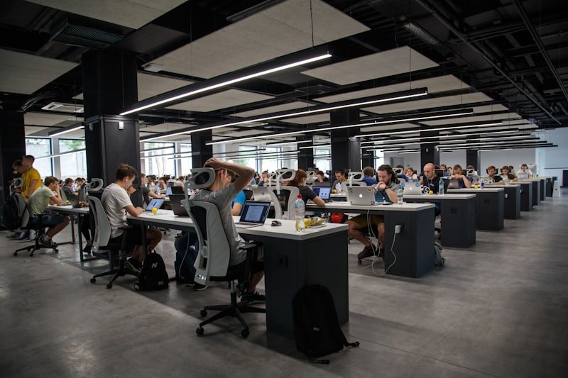 An open-plan office with rows of desks under exposed ceiling services.