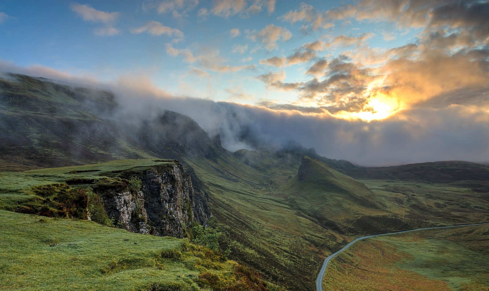 A single road curving through a green valley beneath low cloud.